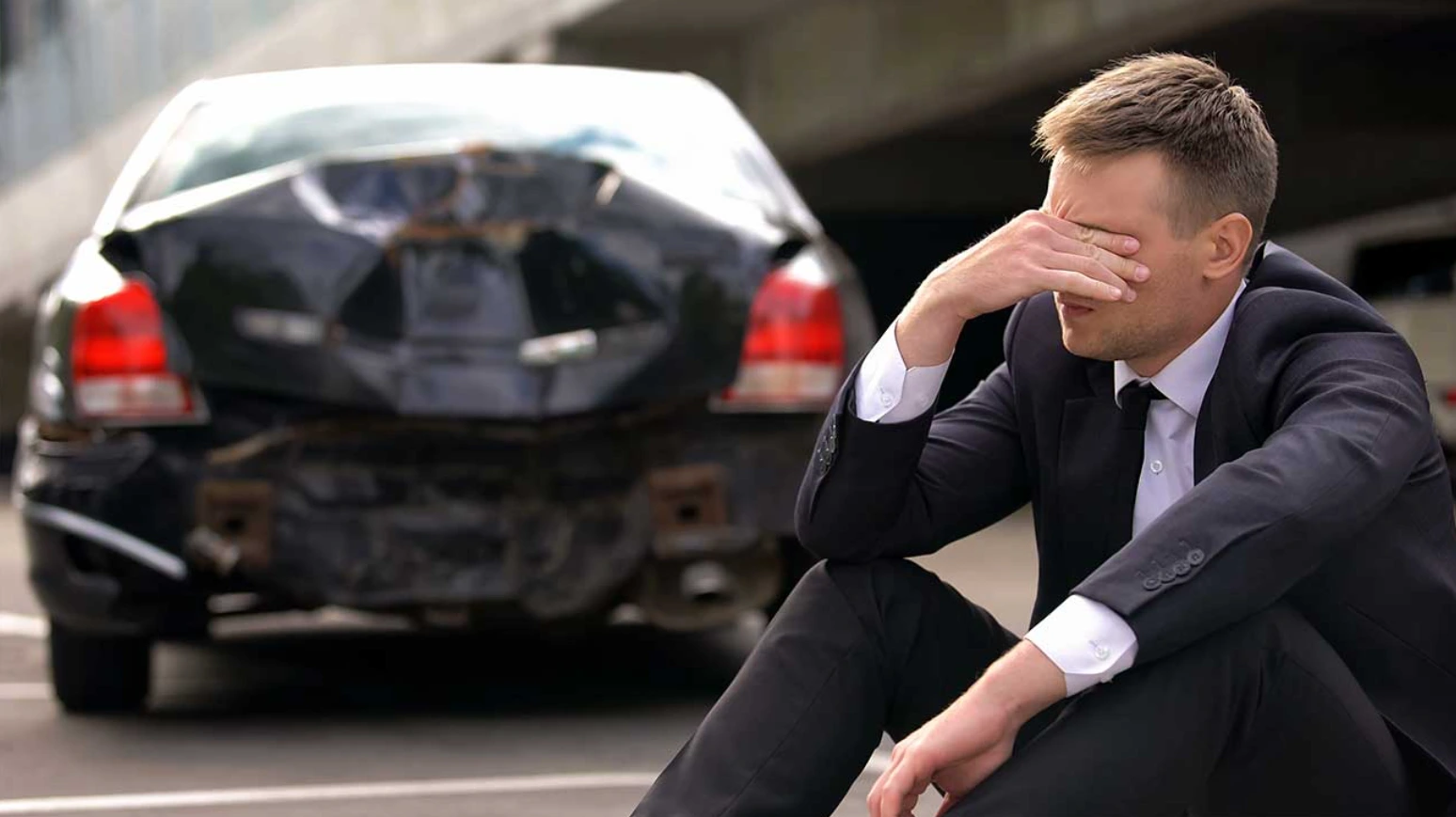 man sitting behind a wrecked car
